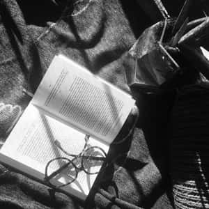黑白布料上打開的書本、眼鏡和植物。