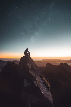 黃昏時分，一個人在星空下的山頂上坐著的剪影。
