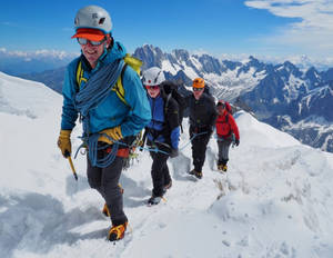 四名登山者正在攀登白雪覆蓋的山脊，身後是積雪的山峰。