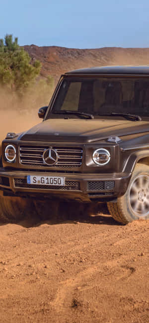 黑色 Mercedes G-Class 在塵土飛揚的沙漠地形中行駛，有丘陵和樹木。