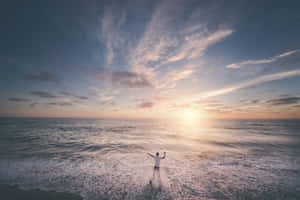日落時分，一個人站在海浪中高舉雙臂