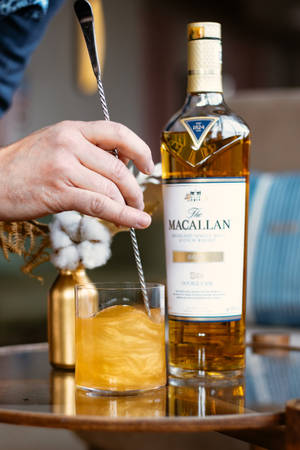 手在Macallan酒瓶旁攪拌威士忌雞尾酒，木托盤
