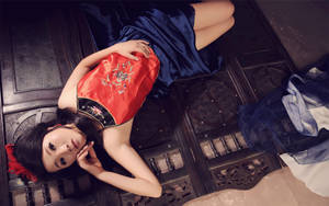 一位身穿紅藍傳統服飾的女性躺在木地板上。