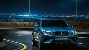 藍色BMW X4概念車在蜿蜒的山路上夜間行駛，下方城市燈光閃爍。