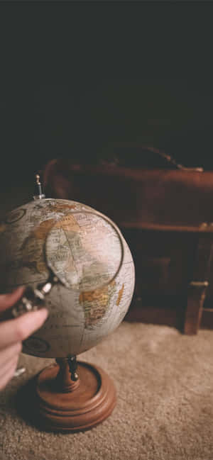 手在復古地球儀上使用放大鏡，旁邊有手提箱。 — 工具 壁紙