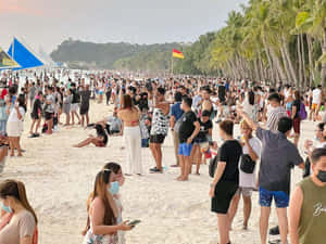 許多人在擁擠的熱帶海灘上戴口罩，有棕櫚樹和帆船。