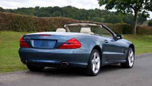 藍色 Mercedes SL500 開篷車停在有草和樹木的道路上。