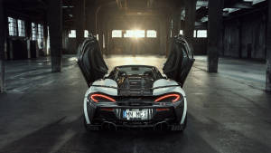 白色McLaren跑車打開車門，停在陽光普照的工業倉庫中。