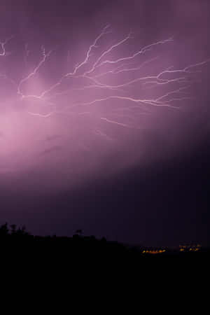紫色閃電劃過黑暗樹線和遠處城市燈光之上的暴風雨夜空。