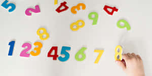 孩子的手在散落的彩色數字磁鐵中拿著一個黃色數字8磁鐵。 — 數學 壁紙