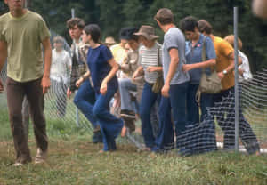 穿著1970年代服裝的年輕人在草地上破損圍欄旁邊行走。