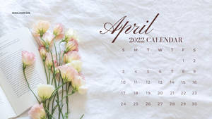 2022年4月日曆，粉紅色花朵和打開的書本在白色布料上。