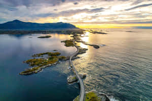 日落時分一條蜿蜒的海岸公路，海面和遠處山脈上反射著金色光芒。 — 道路 壁紙
