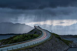 在風暴天空下，一條蜿蜒的道路越過山丘，帶有汽車燈光的條紋。