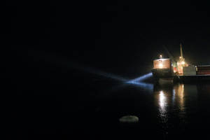 貨船在夜間航行，明亮的燈光反射在平靜的水面上。