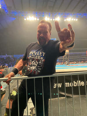 穿著 Bullet Club 襯衫的摔角手在金屬護欄後面向人群做出搖滾手勢。