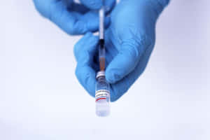 戴藍色手套的手用注射器從藥瓶中抽取疫苗。