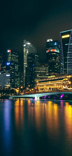 現代城市天際線的夜景，有明亮的建築物和水上的橋樑。
