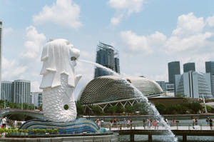 魚尾獅雕像在新加坡城市景觀中噴水，有人和圓頂建築。