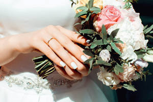 新娘的手拿著一個花束，結婚戒指清晰可見。