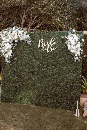 綠色樹籬牆，飾有白色花朵和 bride to be 標誌。