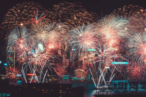 五顏六色的煙花照亮了水面上夜晚的城市景觀。 — 聖誕快樂 GIF 壁紙