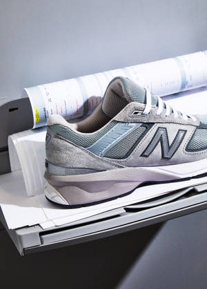 灰色New Balance運動鞋在打印機托盤上，旁邊有捲起的藍圖。 — 卡通鞋 壁紙