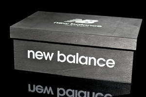 黑色New Balance鞋盒，帶有白色標誌，位於反射表面上。 — 卡通鞋 壁紙