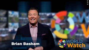 新聞主播 Brian Basham 在帶有色彩繽紛 World Watch 標誌的廣播佈景上微笑。