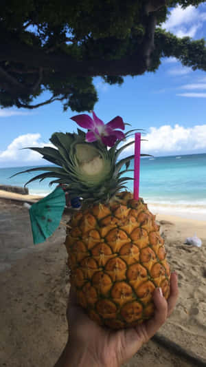 手在沙灘上拿著菠蘿飲品、蘭花和吸管。