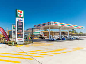 7-Eleven加油站，有Mobil油泵和黃色條紋路面，天空湛藍。