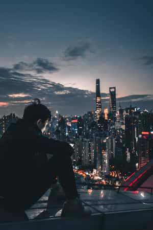 一個人坐在屋頂上，凝視著黃昏時燈火通明的城市天際線。 — 天際線 壁紙
