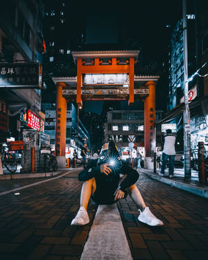 夜晚喺燈光門下蹲喺街上揸住發光電話嘅人。