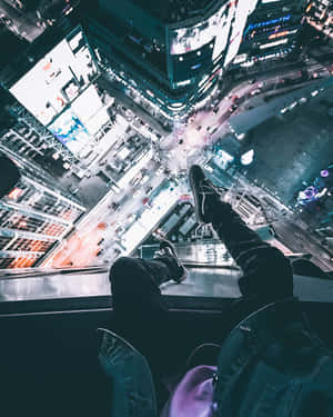 一個人喺高處嘅邊緣放鬆，俯瞰夜晚發光嘅城市。 — 天際線 壁紙