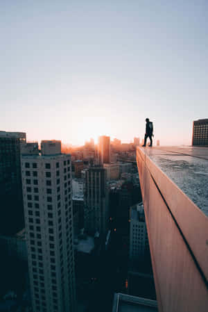 一個人站在屋頂邊緣俯瞰夕陽下的城市 — 天空景觀 壁紙