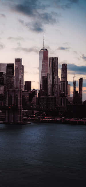 黃昏時分的 One World Trade Center 和布魯克林大橋，天空多雲，下方有水 — HMD Pulse 2 Pro 壁紙