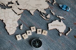 木製世界地圖拼圖同 Scrabble 字母磚拼出 travel，連同指南針。 — 世界地圖 壁紙