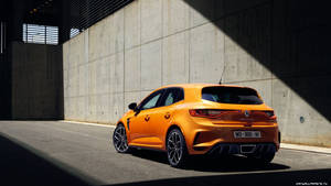 橙色雷諾 Mégane RS 停泊在混凝土牆下，強烈陽光和陰影。