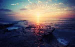 海洋上的夕陽，前景的岩石反射出溫暖的色彩。