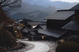 蜿蜒的石徑穿過傳統的日本村莊，背景是積雪的山峰。