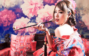 身穿紅色花卉和服的女性在室內抽長煙斗，搭配牡丹壁紙。