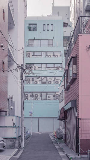 色彩繽紛的建築之間的狹窄小巷，背景是粉藍色的公寓。 — 柔粉 壁紙