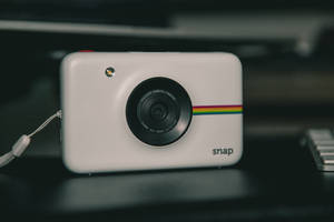 帶有彩虹條紋的白色Polaroid Snap相機，深色桌子上，旁邊有鍵盤。