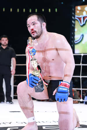 MMA拳手在八角籠中獲勝後跪地手持冠軍獎盃 — 動漫打鬥 壁紙