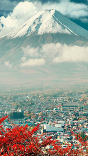白雪覆蓋的富士山俯瞰著一個小鎮，前景有紅色的秋葉。