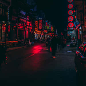 夜晚，一個人在狹窄的城市街道上行走，頭頂是發光的紅色和藍色霓虹招牌。 — 日本 壁紙