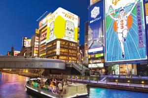 一艘載滿人的運河船在夜間的東京滑過燈火通明的建築物和霓虹招牌。 — 日本 壁紙