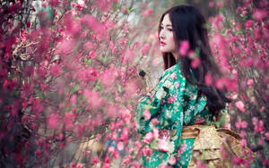 春天花園中，身穿綠色花卉和服的女士被粉紅色花朵環繞。