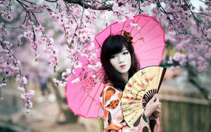 身穿和服的女士在櫻花下拿著粉紅色雨傘和扇子。 — 櫻花 壁紙