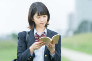 一位穿著制服的年輕學生在草地小徑上戶外閱讀一本書。